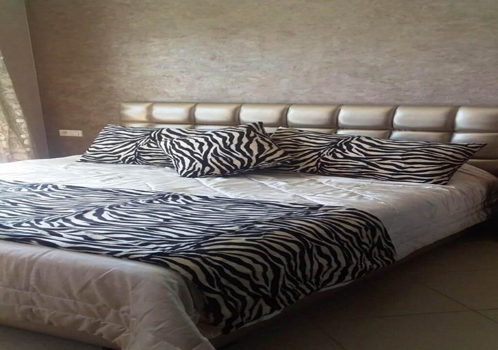 Una cama con colcha y almohadones estampados con diseño de cebra, un cabecero capitonado y una pared lisa.