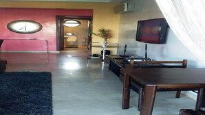Una sala de estar moderna con un televisor grande, una mesa de centro y un sofá. Hay una mesa de comedor con sillas y una alfombra en el suelo.