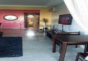Una sala de estar moderna con un televisor grande, una mesa de centro y un sofá. Hay una mesa de comedor con sillas y una alfombra en el suelo.