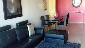 Una sala moderna con un sofá de cuero negro, una mesa de centro de vidrio y una mesa de comedor con sillas.