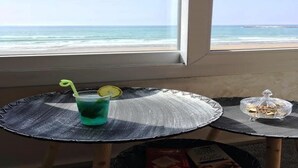 Une table avec une boisson et un récipient contenant des en-cas, placée près d’une fenêtre donnant sur la plage.