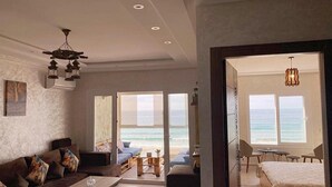 Un vaste espace de vie avec une grande fenêtre donnant sur la mer, un coin salon confortable avec un canapé et des fauteuils, et une chambre séparée avec un lit et vue sur l’océan.