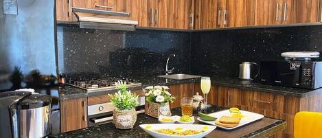 A modern kitchen with wooden cabinets, a black countertop, a stainless steel refrigerator, a coffee maker, and a yellow chair.
