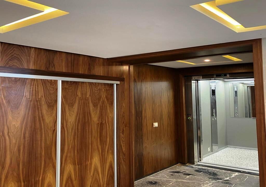A modern elevator with a glass door, surrounded by wooden paneling and a marble floor.