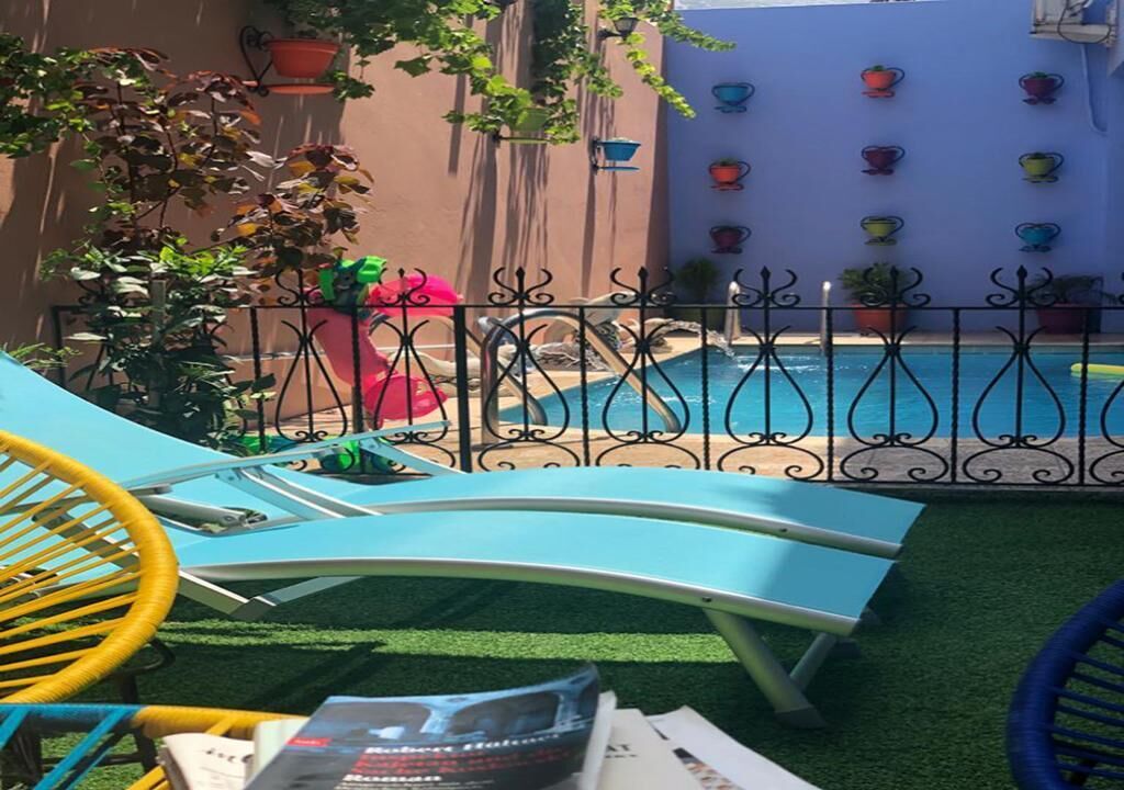 Uma área de piscina com espreguiçadeiras, uma piscina pequena e plantas em vasos.