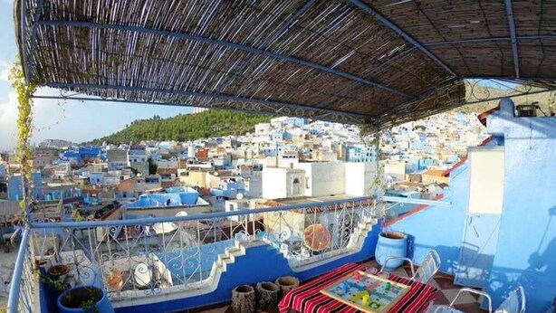 A terrace with a checkered floor, a table with chairs, and a view of a densely packed town with blue buildings. - Duplex in Chefchaouen 5264 (Chefchaouen)