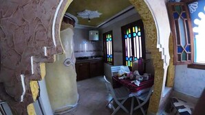 A room with a stone wall, a window with stained glass, and a chair with a striped cushion. - Duplex in Chefchaouen 5264 (Chefchaouen)