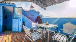 Een overdekt terras met een blauwe muur, een muurschildering en uitzicht op zee.