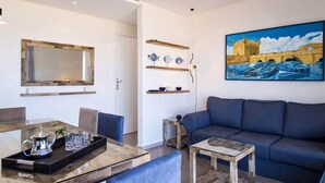 A modern living room with a sofa, a coffee table, a dining table with a tray, a painting of a bridge, and shelves with decorative items. - Splendid Sea View Apartment in Essaouira 5274 (Essaouira)