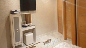 Un dormitorio con cama, armario, escritorio con espejo y televisión en la pared.
