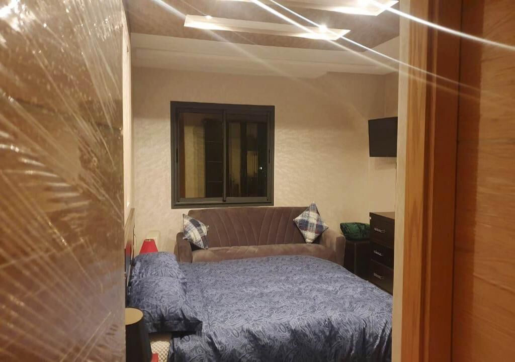 Een slaapkamer met een bed, een raam, een dressoir en een televisie aan de muur.