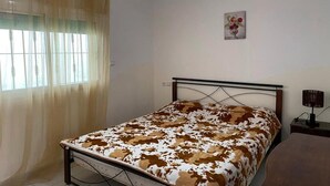 A bedroom with a bed, a bedside table, a lamp, and a window with curtains. - Floor villa in Sidi Bouzid 5283 (Sidi Bouzid)