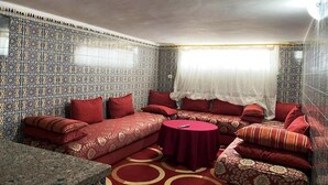 A room with patterned walls, a red sofa set, a round table, and a window with a white curtain. - Floor villa in Sidi Bouzid 5283 (Sidi Bouzid)