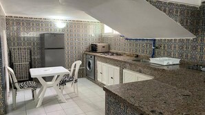 A compact kitchen with patterned tiles, a refrigerator, a microwave, a washing machine, and a dining area with chairs. - Floor villa in Sidi Bouzid 5283 (Sidi Bouzid)