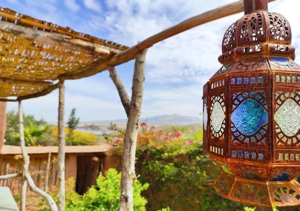 A traditional lantern with intricate designs, a wooden pergola, and a natural landscape with greenery and a distant view.