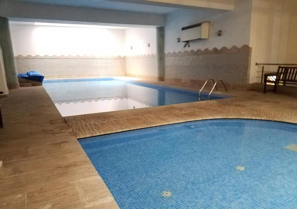 Una piscina interior con paredes de azulejos y una zona de terraza de madera.