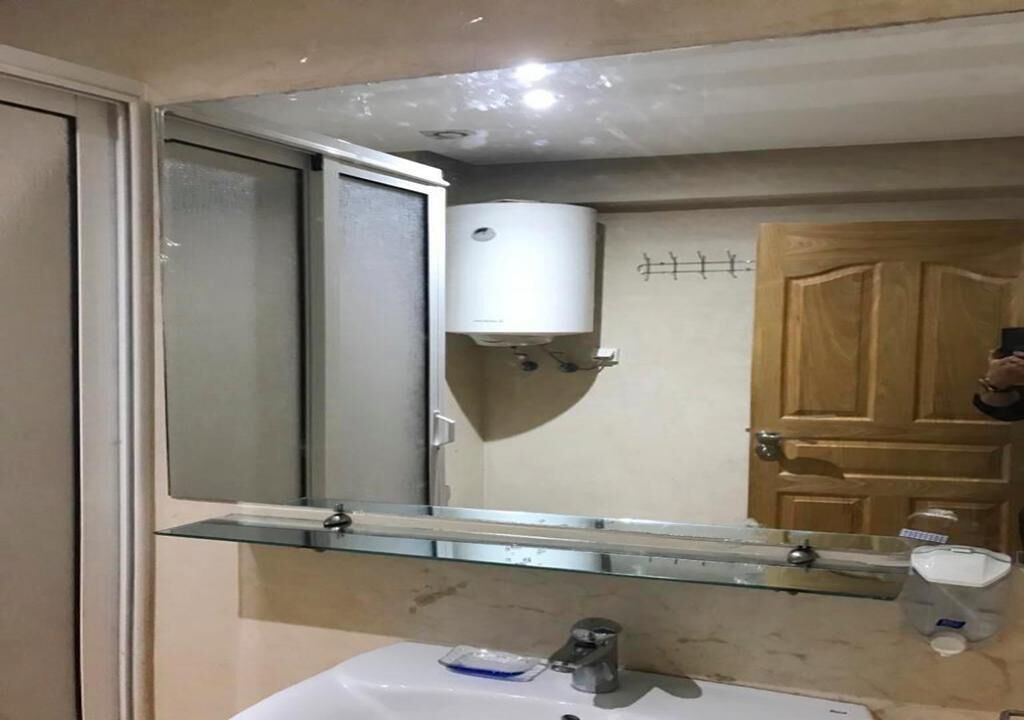 A bathroom with a mirror, a sink, a toilet, and a wooden door.