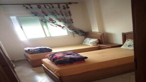 Una camera da letto con due letti singoli, una finestra con tenda e pavimento piastrellato.