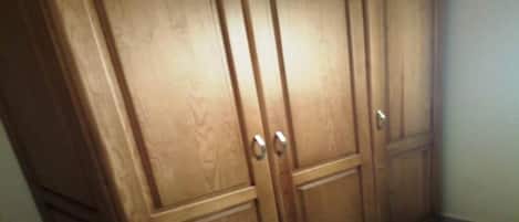 A wooden wardrobe with two doors and a shelf, located in a corner of a room with tiled flooring.