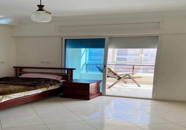A bedroom with a bed, a nightstand, and a sliding glass door leading to a balcony with outdoor furniture. - Sea view apartment in El Hoceima 5329 (El Hoceima)