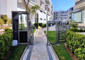 Ein moderner Hotelzugang mit einem Weg zum Gebäude, einem Schild mit dem Schriftzug 'Jasmine' und einem gepflegten Gartenbereich.