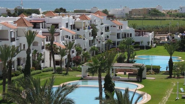 Ein Resort mit mehreren weißen Gebäuden, Palmen und zwei Swimmingpools.