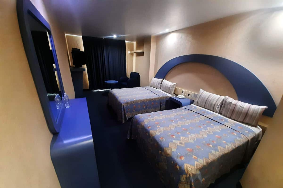 A hotel room with two beds, a desk, a chair, and a small table.