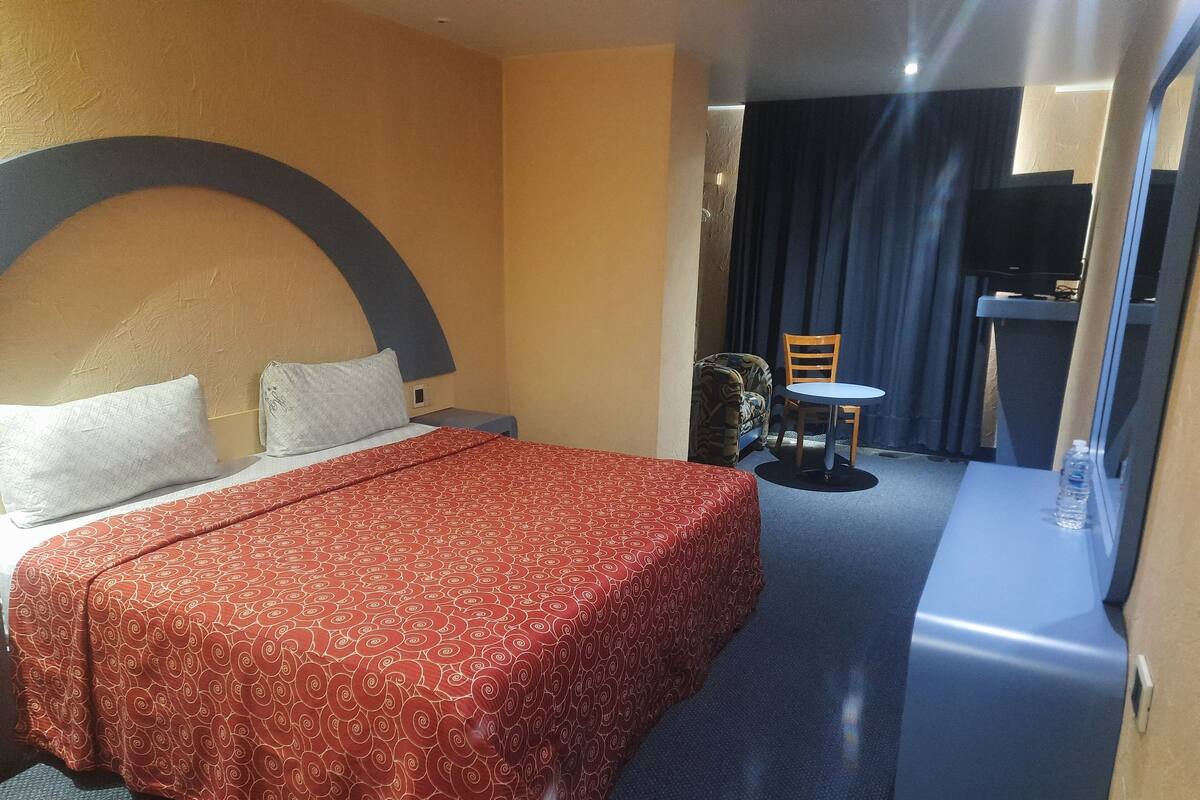 A hotel room with a bed, a small table, a chair, and a TV.