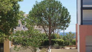 A building with a large tree in front, a clear view of the sea, and a balcony with a railing. - Corbo apartment (Lagos)
