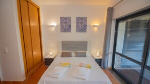 A hotel room with a large bed, two wall-mounted light fixtures, a window with blinds, and a door. - Corbo apartment (Lagos)
