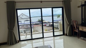 Habitación de hotel con un amplio ventanal corredero que da a un balcón, una cama, un escritorio con una silla y una lámpara.