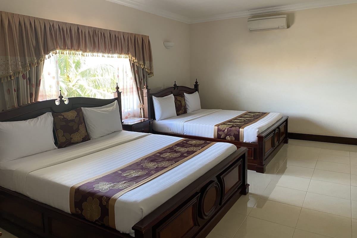 A hotel room with two beds, a window with curtains, a wall-mounted air conditioner, and a tiled floor.