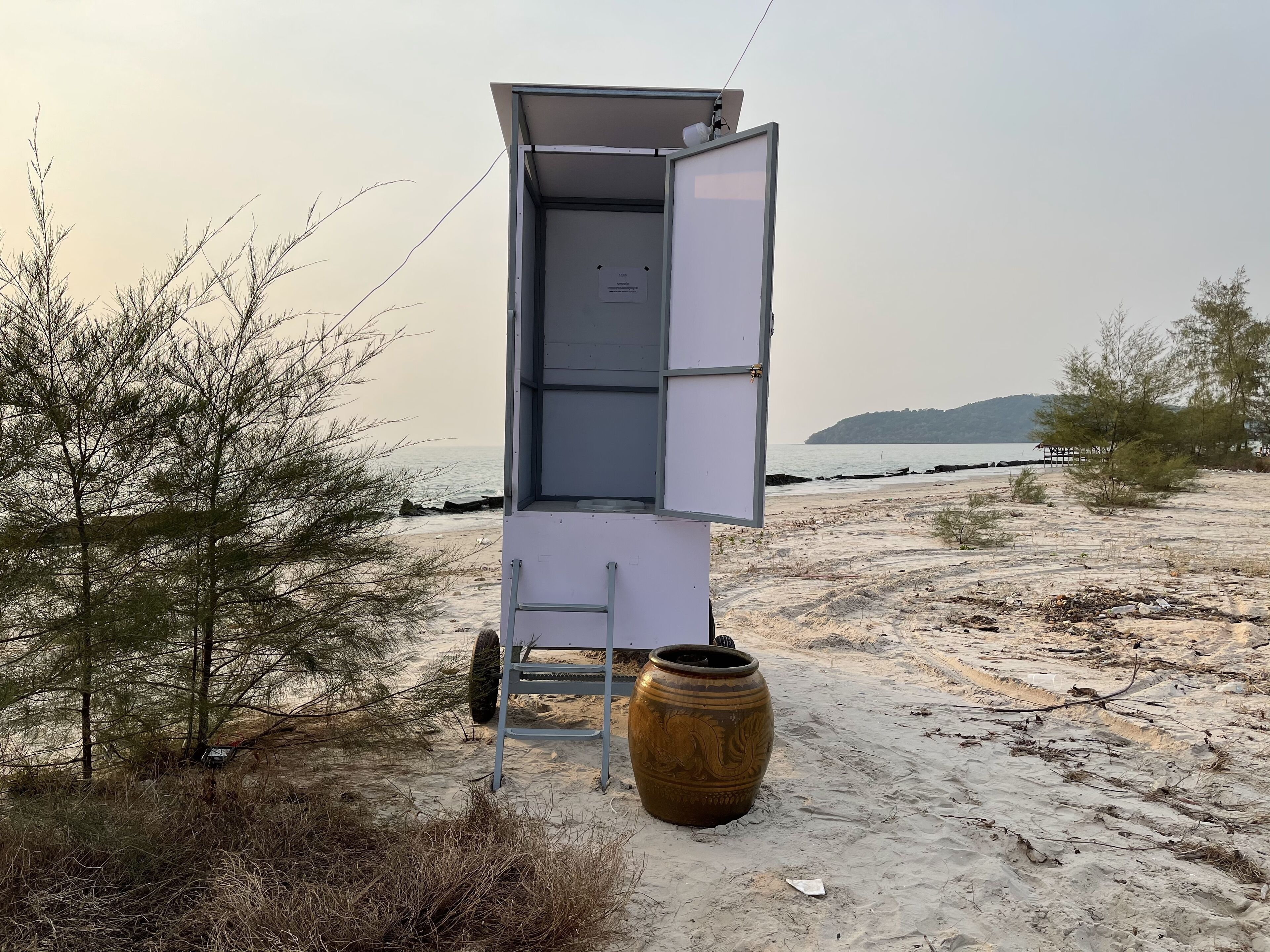 A beachside lifeguard tower with an open door, a ladder, and a large decorative vase.