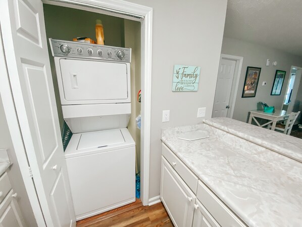 A laundry room with a stacked washer and dryer, a countertop with a sink, and a wall with a 'Family' sign.