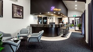 Un área de recepción moderna con un mostrador negro curvo, asientos grises y un letrero de neón que dice "Treasure".