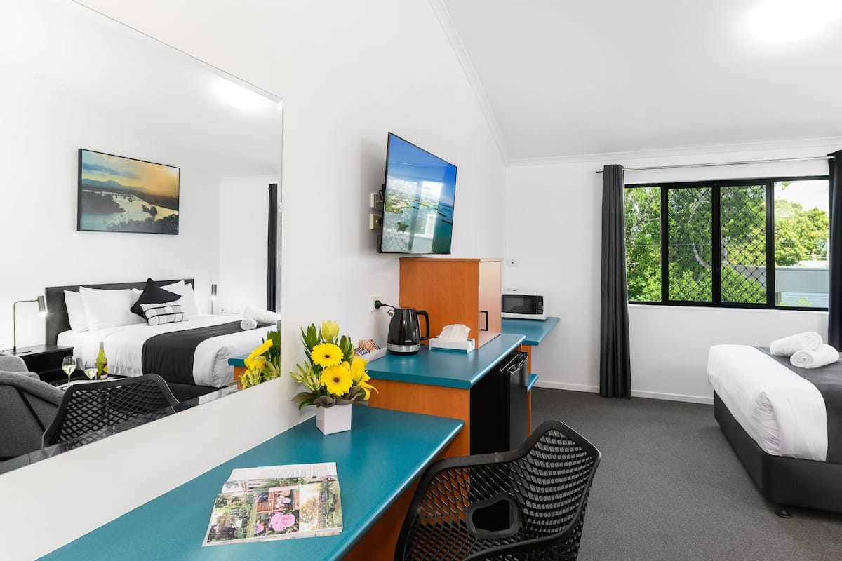 A hotel room with a bed, desk, chairs, a coffee machine, a TV, and a window with a view.