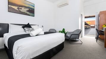 Ein Hotelzimmer mit einem großen Bett, einem Schreibtisch mit Stuhl, einer Zimmerpflanze und einem Bild an der Wand.