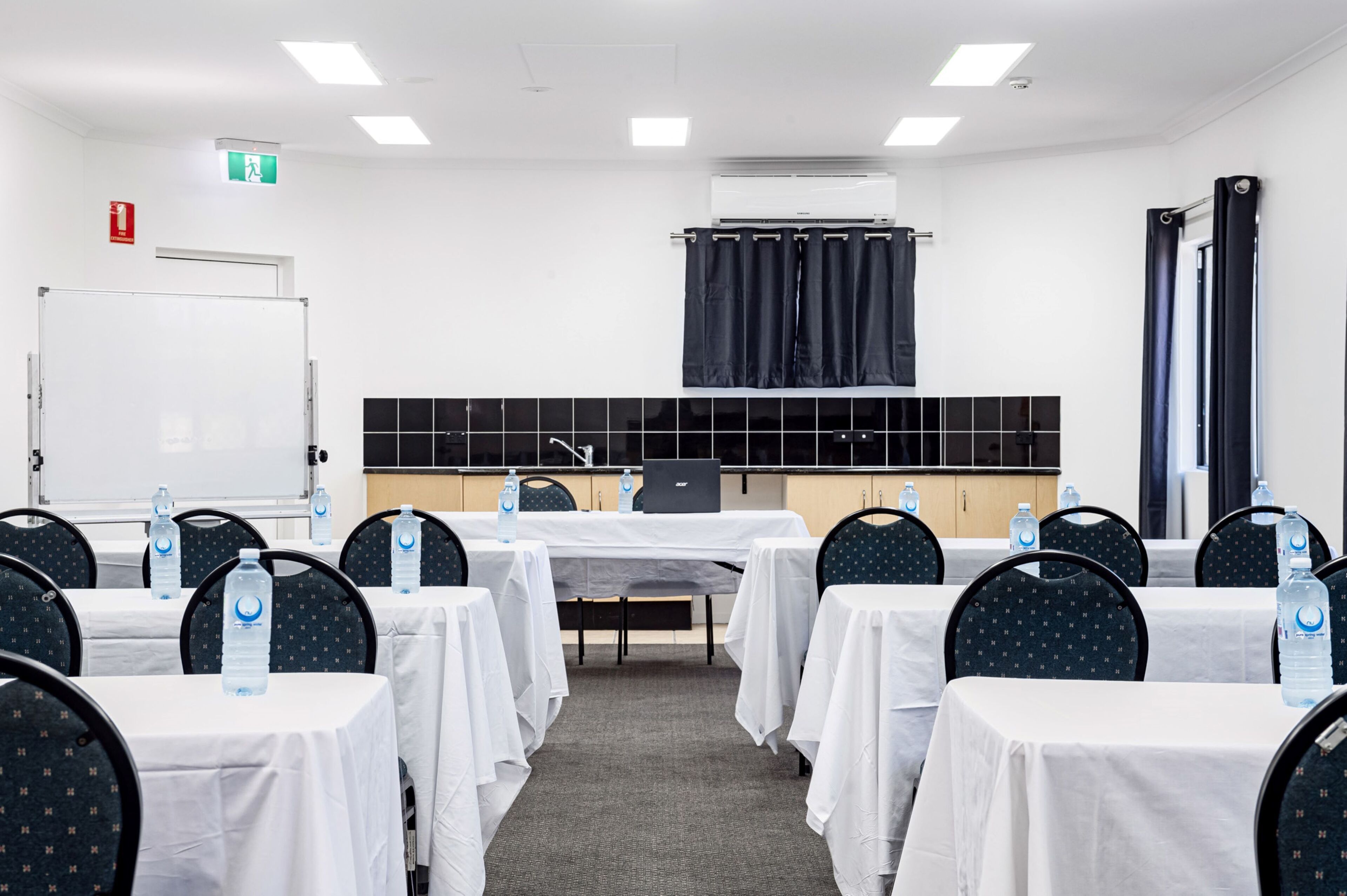 A conference room with tables, chairs, a whiteboard, and an air conditioning unit.