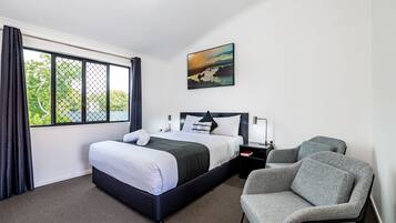 Una habitación de hotel con una cama, una silla, una mesita de noche y un cuadro en la pared.