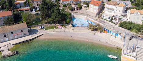 An aerial view of a coastal town with buildings, a beach, and a clear blue sea.