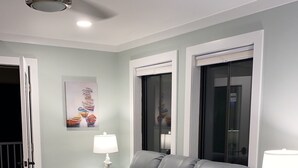 Un salon moderne avec un canapé d’angle gris, deux lampadaires et un ventilateur de plafond.
