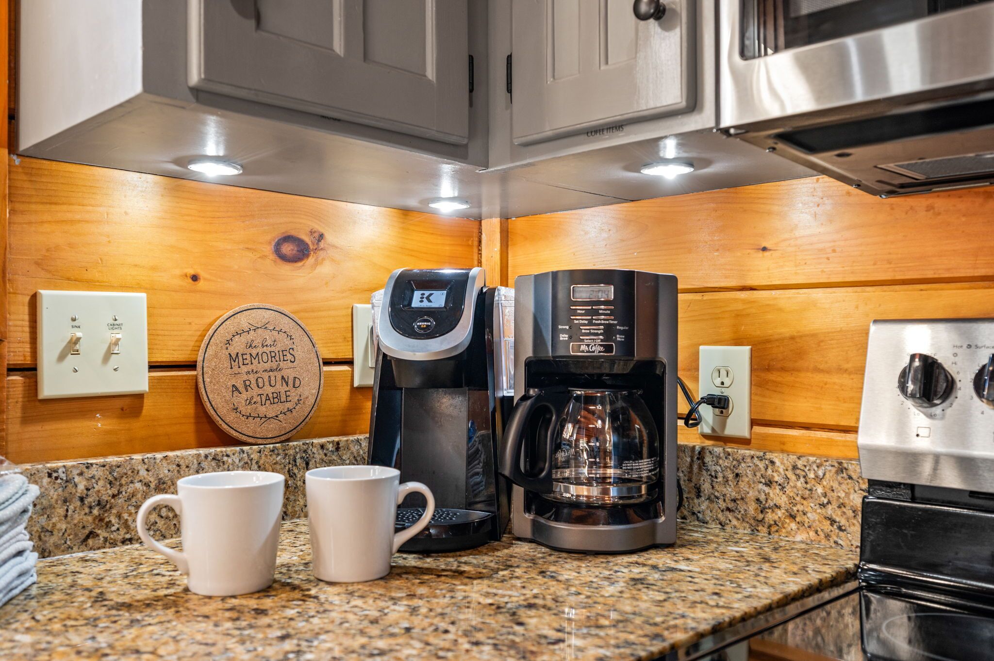 Una cocina con cafetera, dos tazas y un reloj de pared.