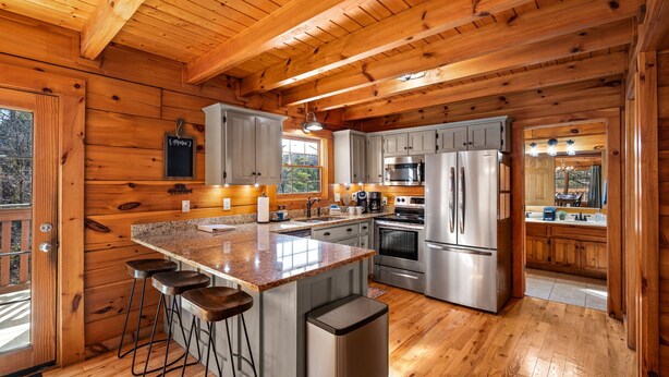 A wooden cabin kitchen with a granite countertop, stainless steel appliances, and a bar stool area. - 3BR Cabin: Hot Tub, Arcade & Game Room, Near Strip (Pigeon Forge)