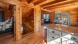 A wooden cabin interior with a dining area, kitchen, and a bedroom with a bed and nightstand. - 3BR Cabin: Hot Tub, Arcade & Game Room, Near Strip (Pigeon Forge)