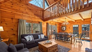 A cozy wooden cabin interior with a living room, dining area, and a loft bedroom. - 3BR Cabin: Hot Tub, Arcade & Game Room, Near Strip (Pigeon Forge)