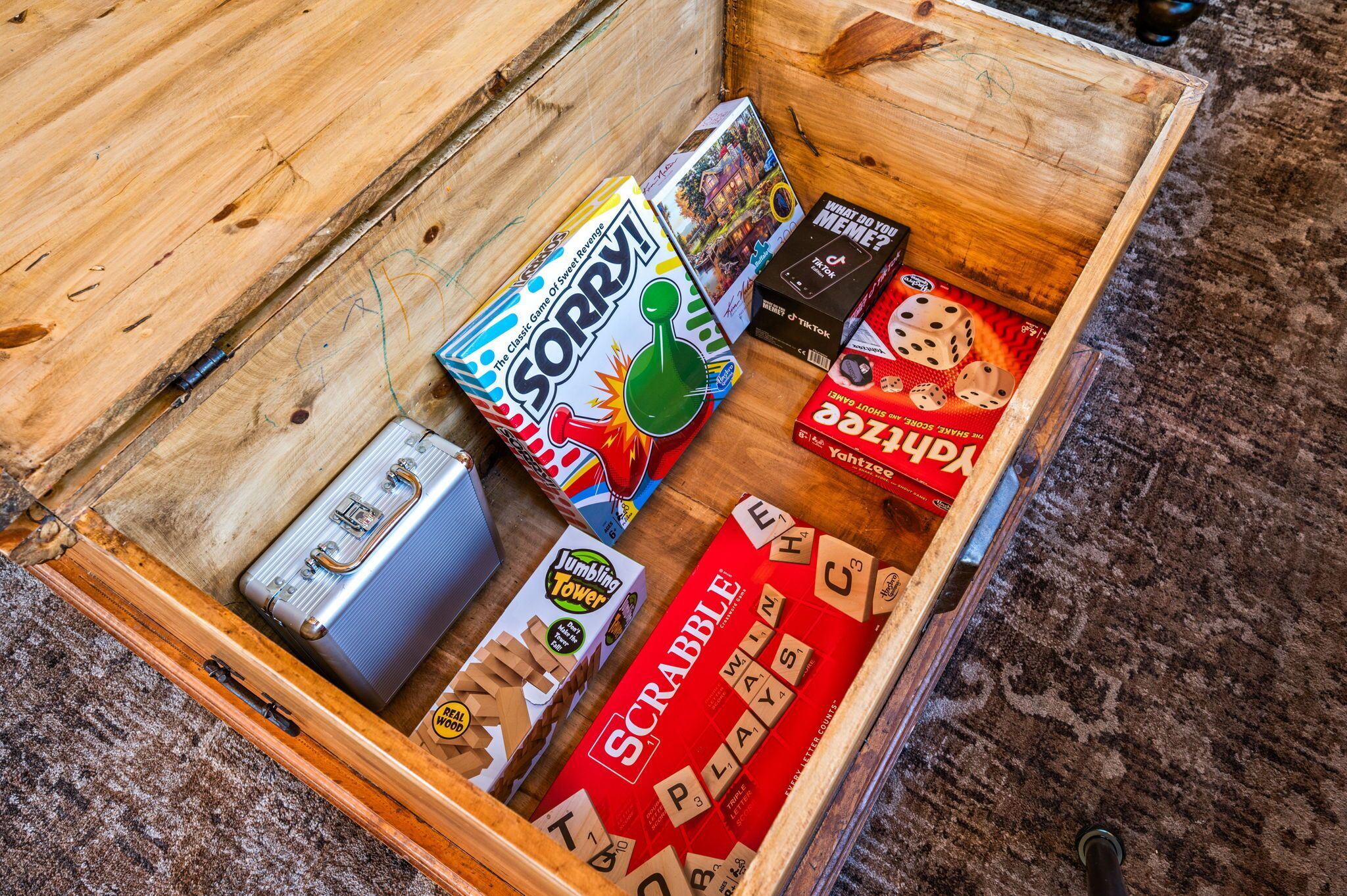 A wooden box containing various board games including Sorry!, JUMBLING TOWER, and Scrabble.