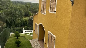 A yellow building with stone steps, a white fence, and a garden with a statue and potted plants.