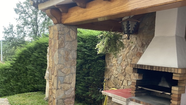 An outdoor brick oven barbecue area with stone pillars, a tiled floor, and a wooden pergola overhead.