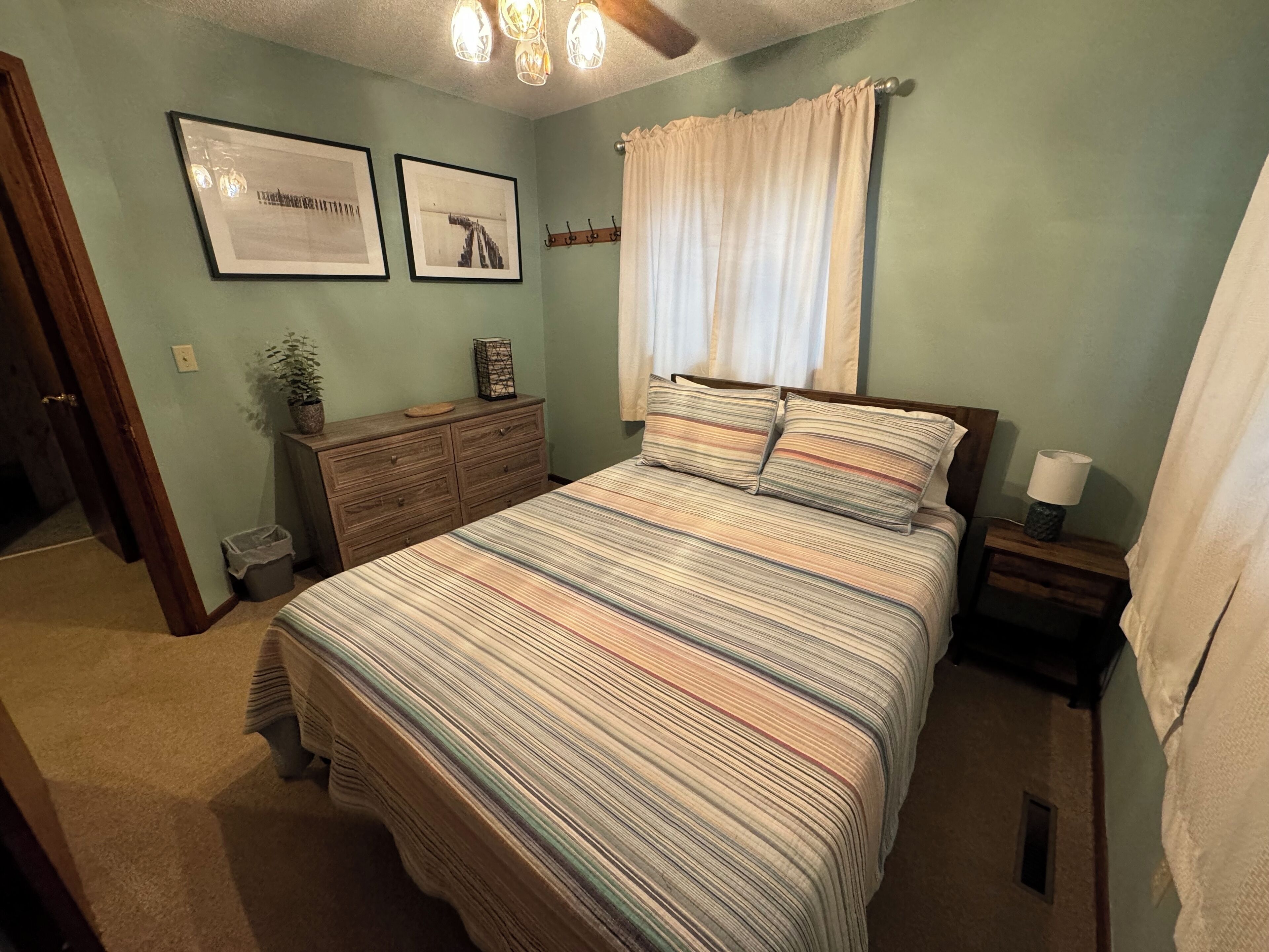 A bedroom with a large bed, a dresser, a nightstand, a lamp, and two framed pictures on the wall.
