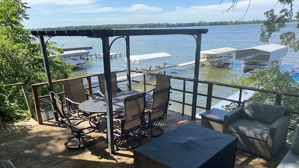 Una terraza de madera con mobiliario exterior, un espacio de estar cubierto y vistas al lago.